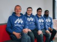 Vier Gründer seitzen auf einer Bank nebeneinander. Alle haben einen blauen Hoodie an mit der Aufschrift und dem Logo von Mitgant in blau. V.l.n.r. Dr. Thomas Fricke, Nils KArn, Dr. Muhammad Sukmana und Kennedy Torkura