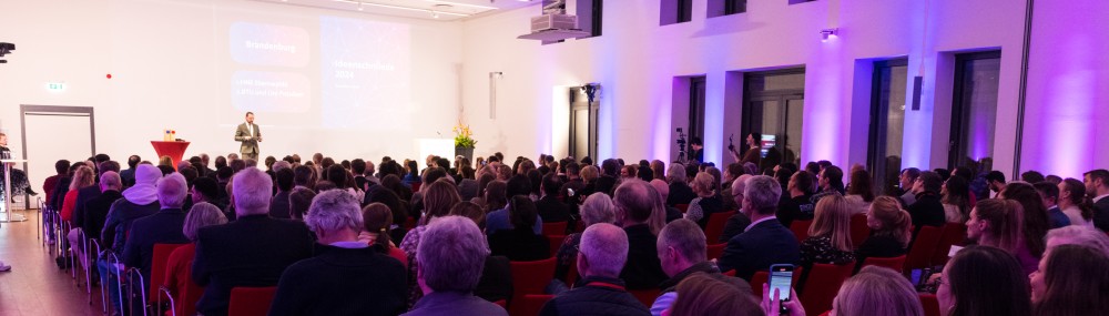 Ein Saal voller sitzender Menschen, von hinten